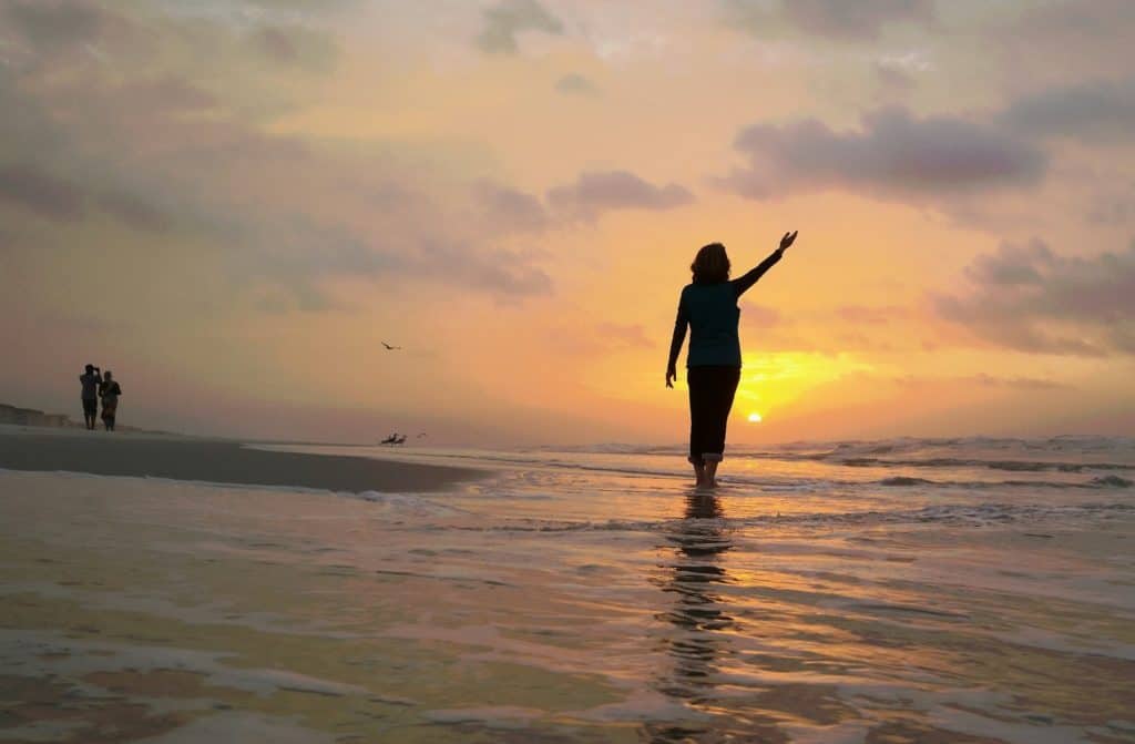 Beach landscape at sunrise with silhouetted confident woman lifting hand to the heavens at beach.