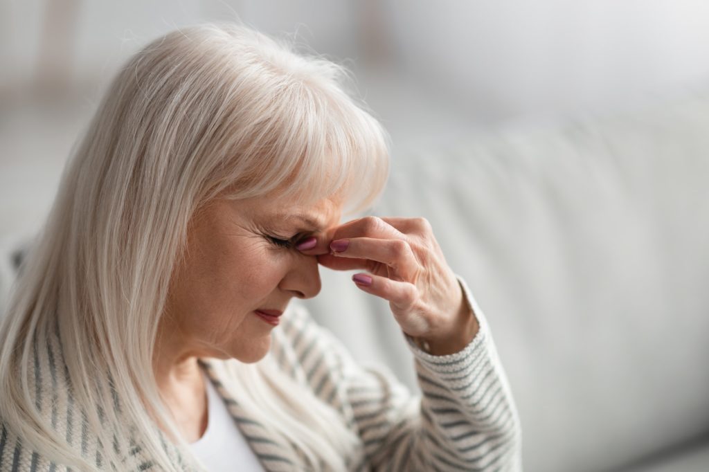 Fatigued upset older woman massaging nose bridge