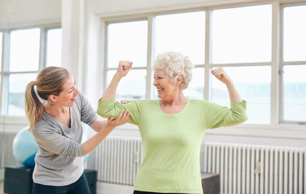 Proud elderly woman flexing her bicep with personal trainer