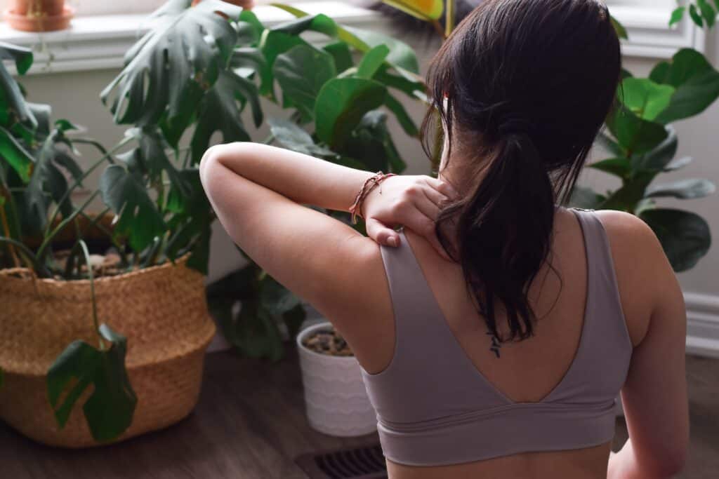 Young woman from behind touching stretching sore neck muscles during workout at home
